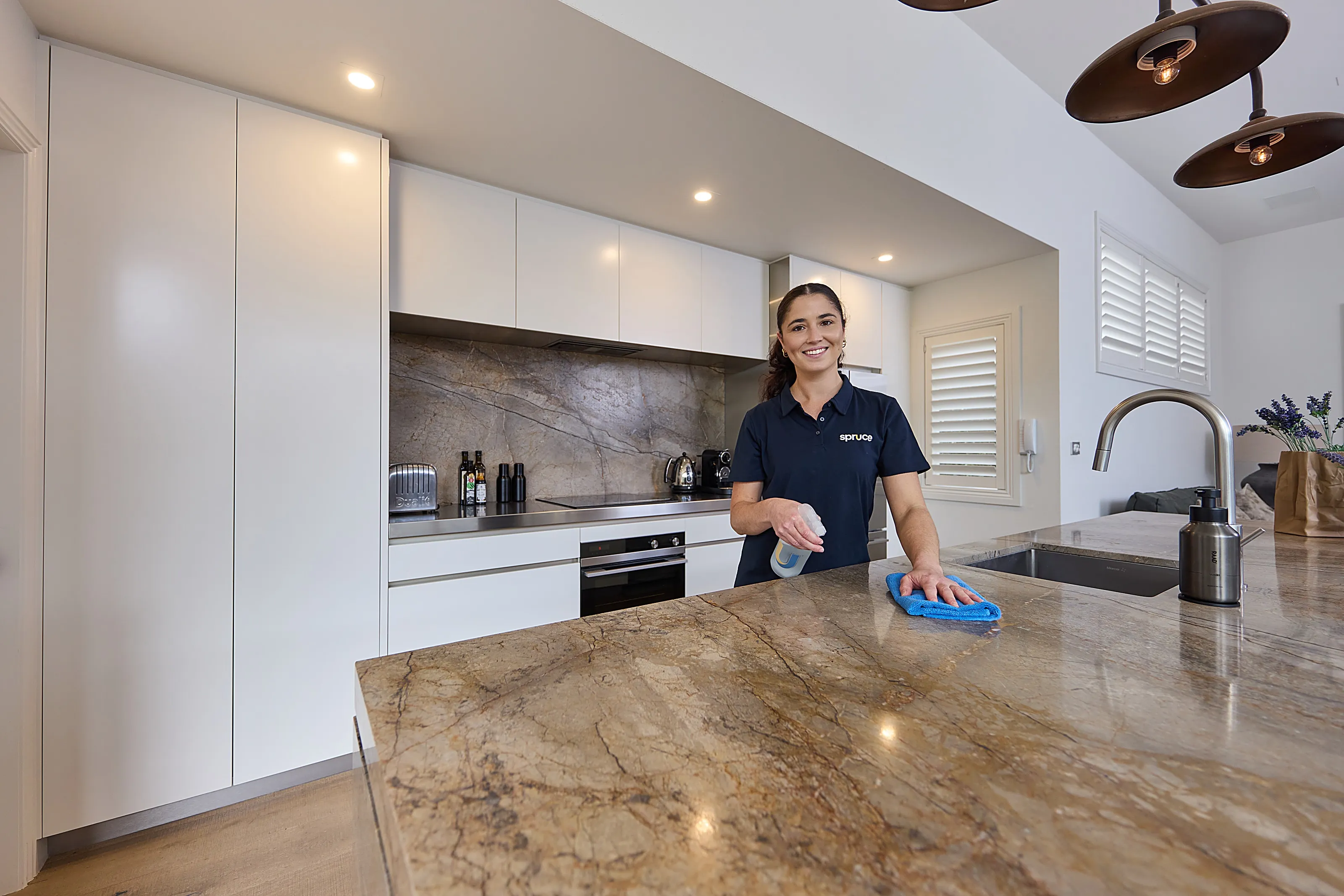 A Spruce cleaner wiping a kitchen benchtop in a bright, modern Wellington home