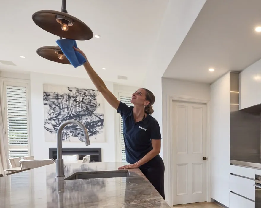 A Spruce cleaner wiping a kitchen light fitting during an end-of-tenancy clean in an Auckland home
