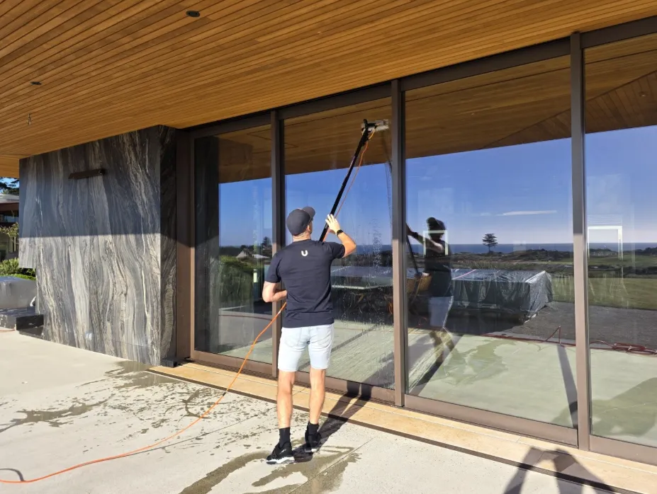 A Spruce cleaner cleaning exterior glass doors with a squeegee pole at a New Zealand home