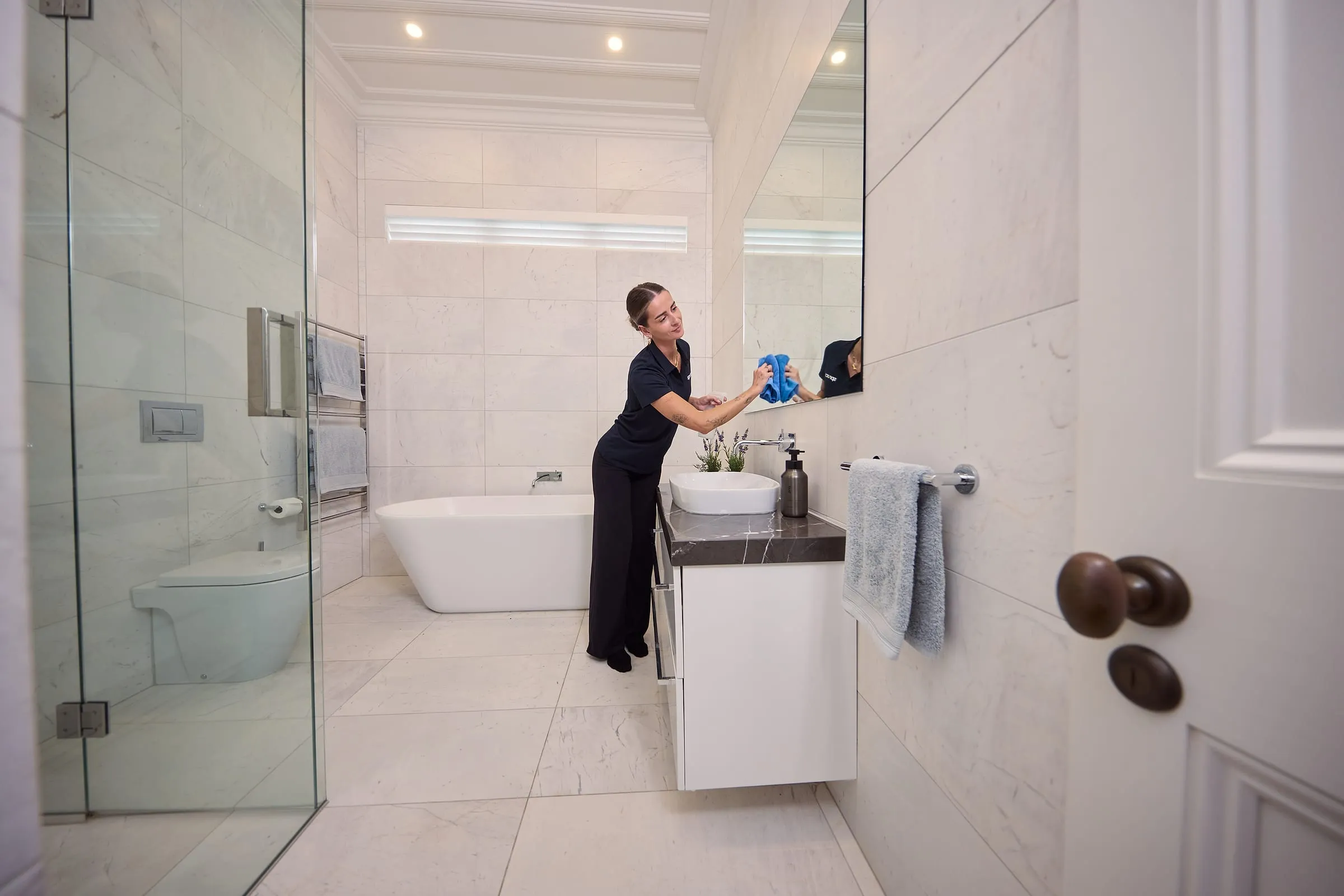 A Spruce cleaner polishing the mirror in a bright marble bathroom in a Wellington home