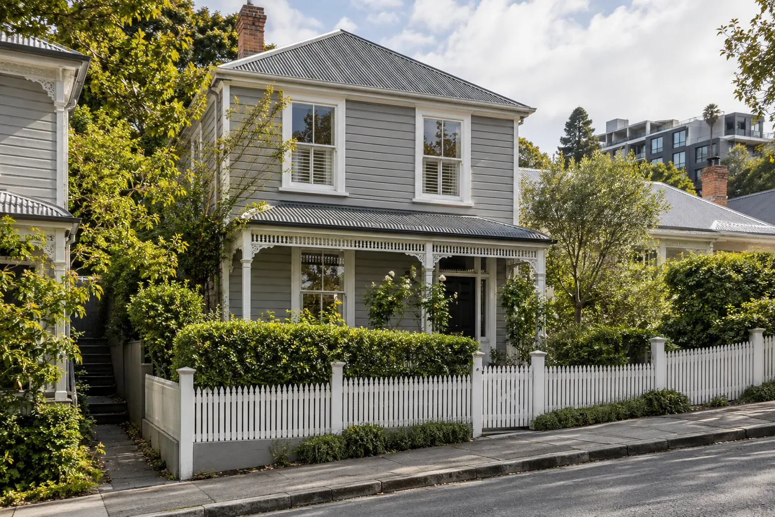 A two-storey heritage weatherboard villa behind a white picket fence on a leafy Parnell street