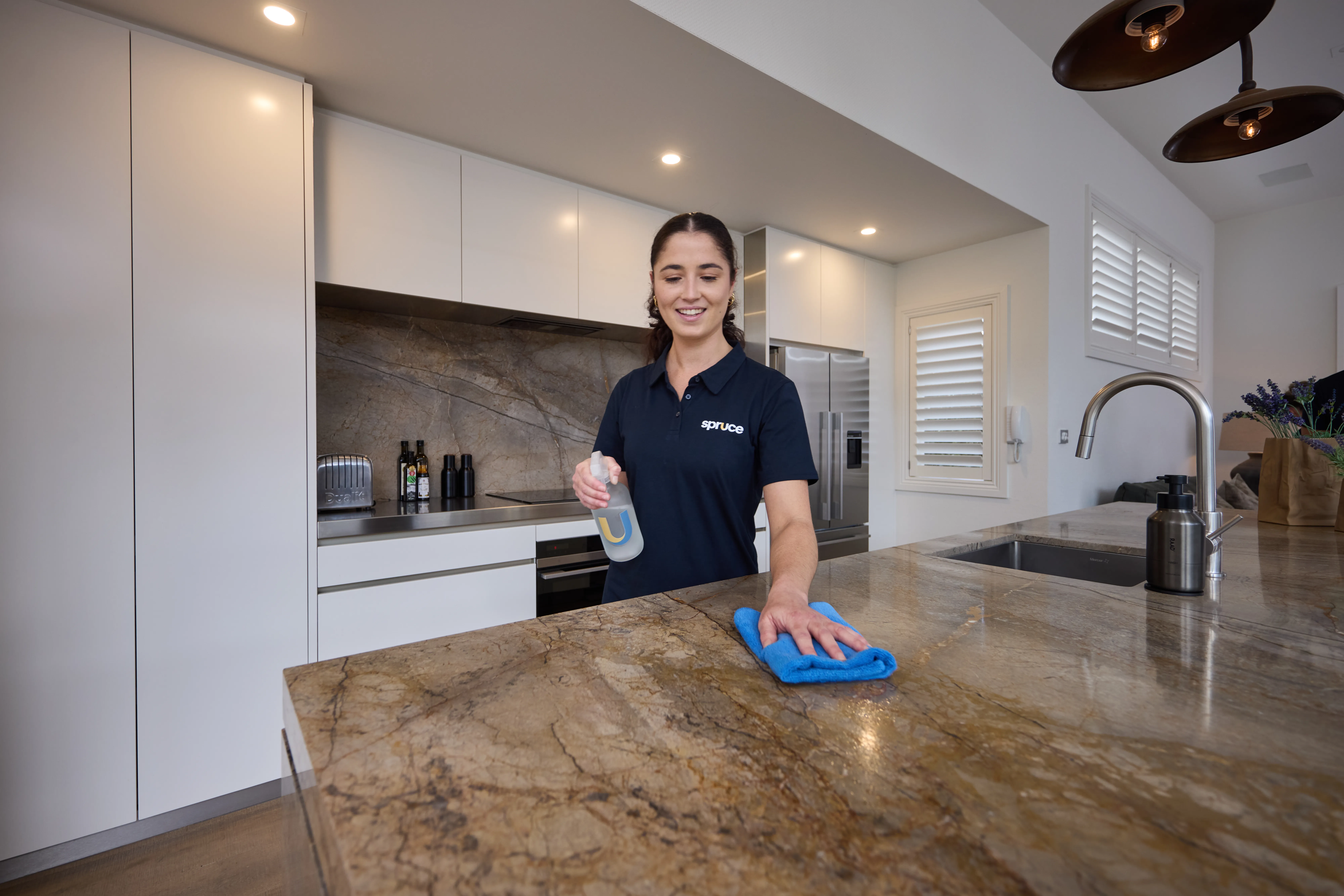 A Spruce cleaner wiping a marble kitchen benchtop during a regular clean in an Auckland home