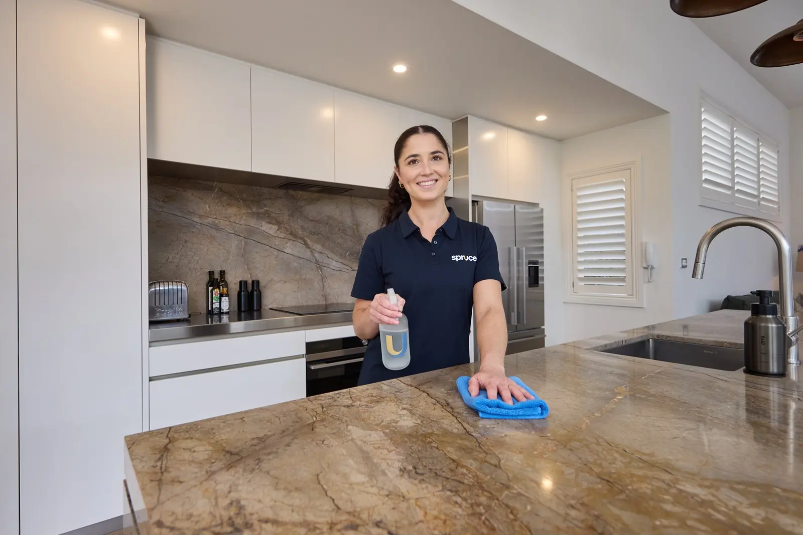 A Spruce cleaner wiping down a kitchen benchtop in a New Zealand home