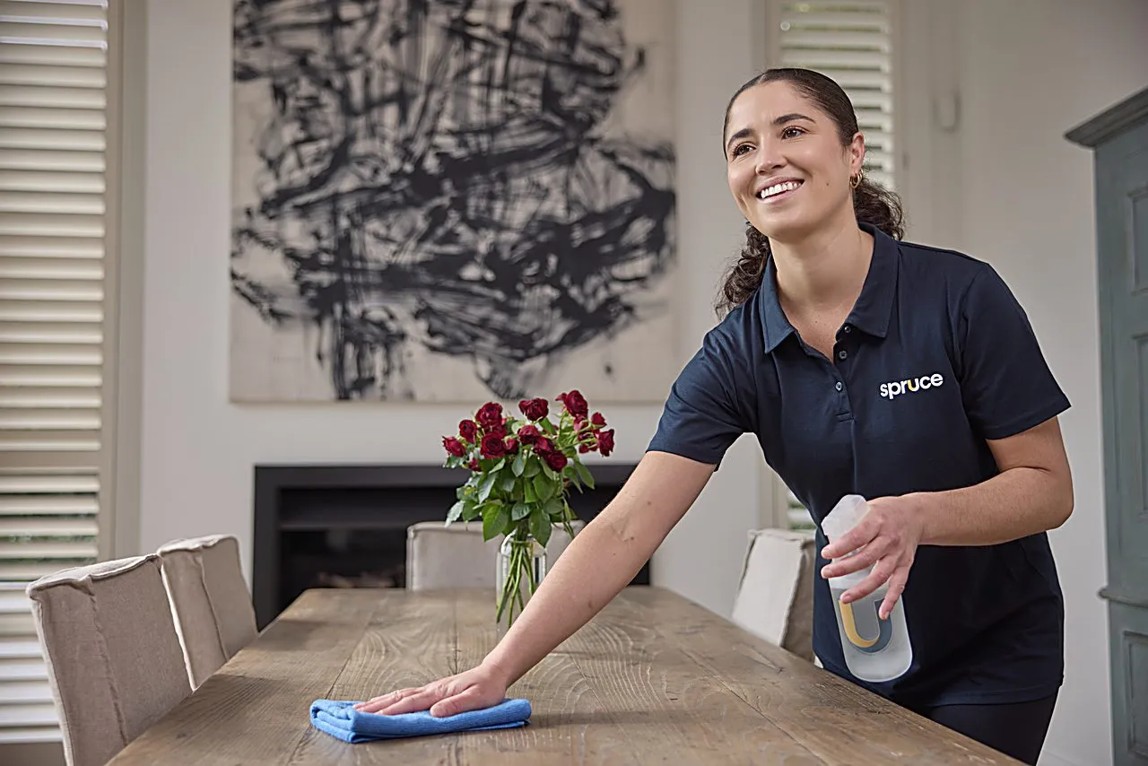 A Spruce cleaner wiping down a dining table in a bright New Zealand home
