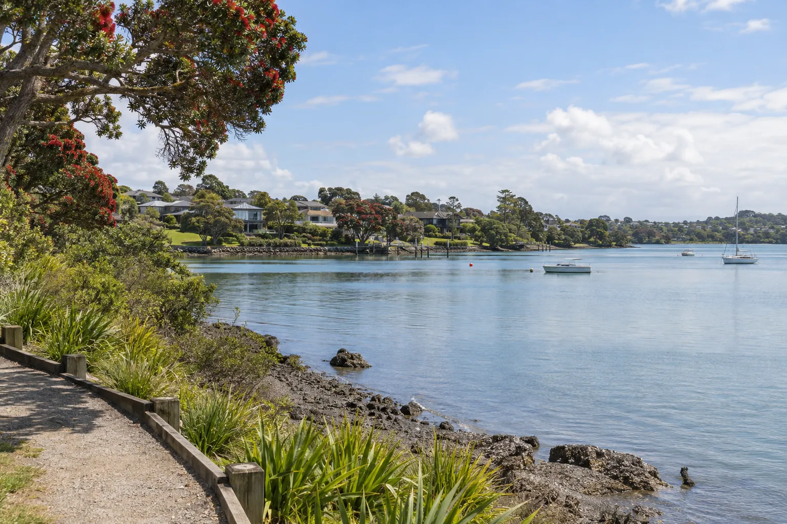 Coastal walkway, homes and pōhutukawa beside the Upper Harbour at Whenuapai
