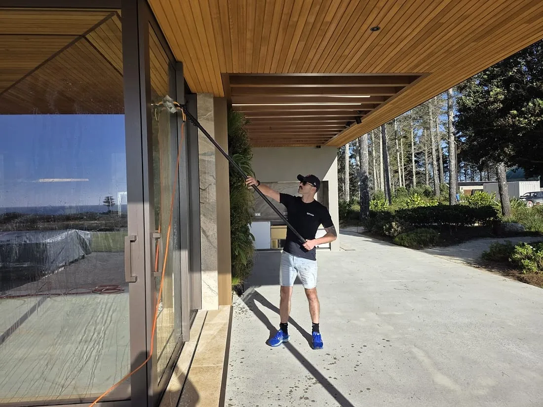 A Spruce technician cleaning exterior glass doors with a pure-water pole at a modern Wellington home
