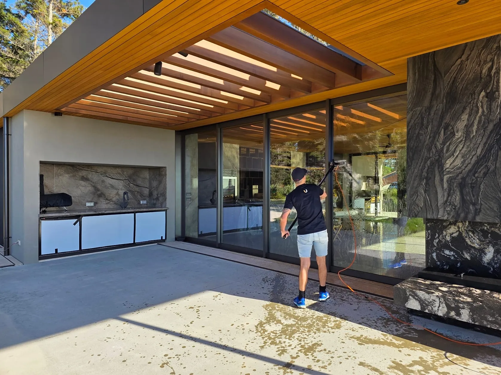 A Spruce technician cleaning large exterior glass doors with a pure-water pole at a modern Wellington home