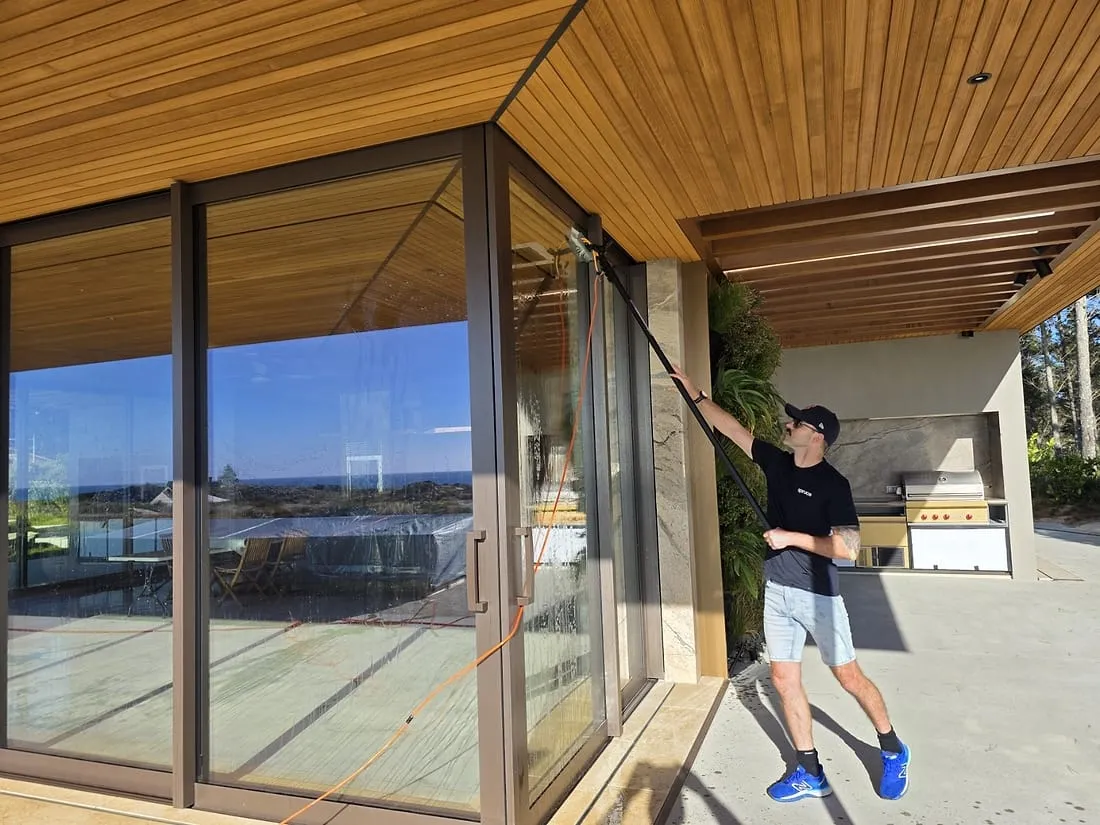 A Spruce technician washing floor-to-ceiling windows with a pure-water pole at a Wellington home